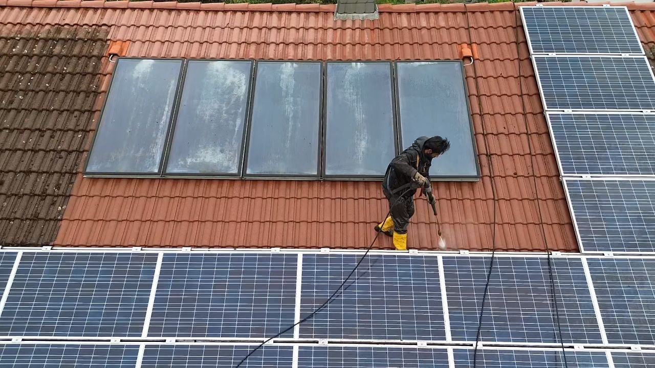 Luftaufnahme einer professionellen Dachreinigung: Ein Mitarbeiter säubert mit einem Hochdruckreiniger ein stark verschmutztes Ziegeldach. Der Kontrast zwischen der gereinigten, roten Fläche und dem dunklen Moosbefall ist deutlich sichtbar.