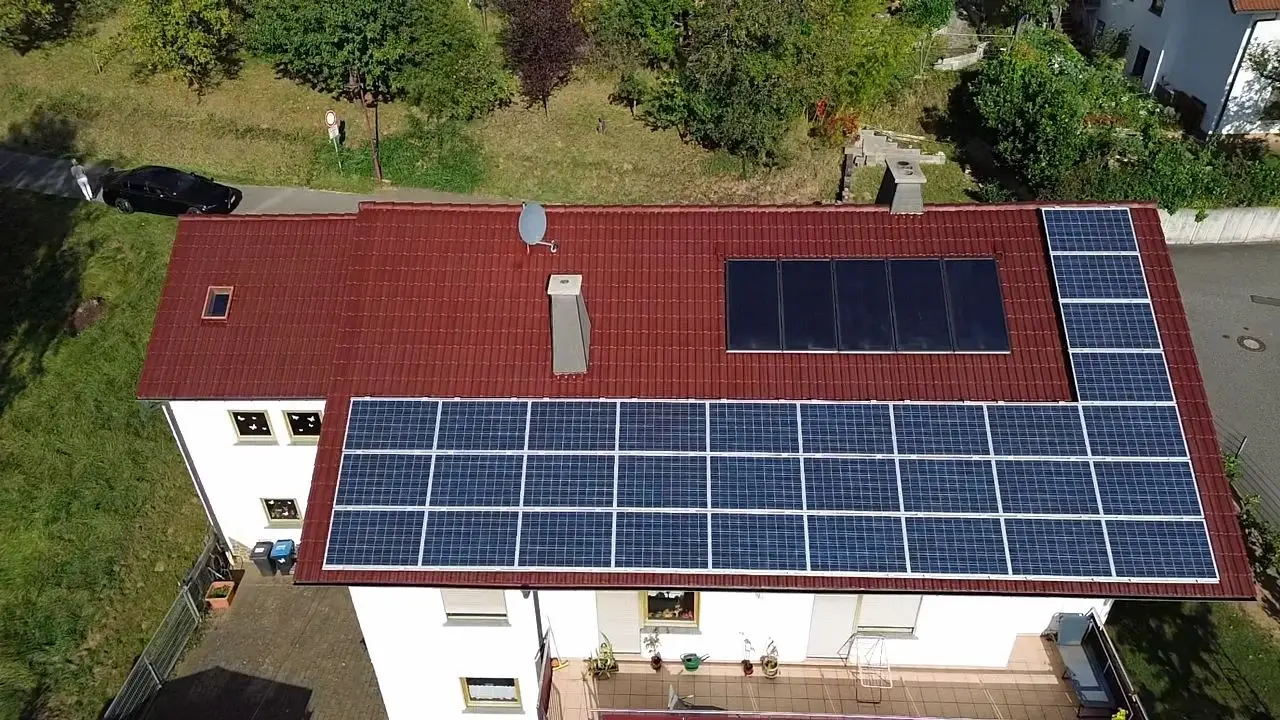 Luftaufnahme eines roten Ziegeldachs mit einer großflächigen Photovoltaikanlage und zusätzlichen Solarthermie-Modulen.