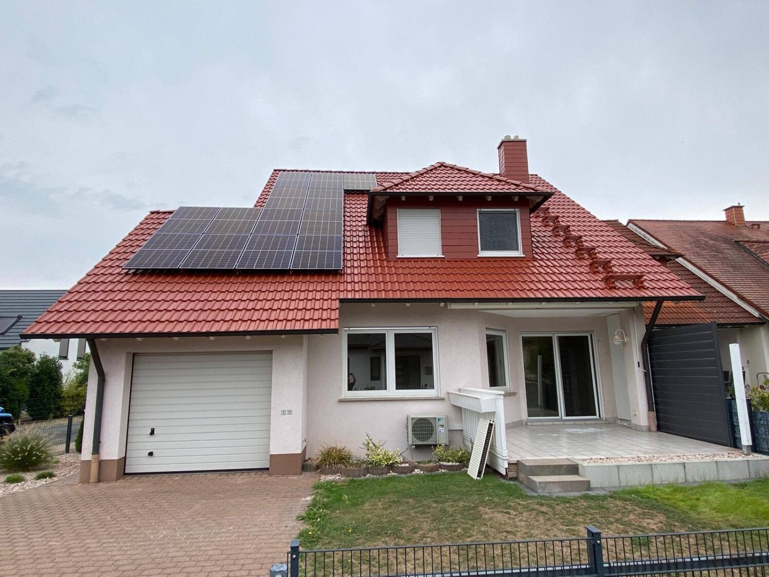 Ein modernes Einfamilienhaus mit einer frisch sanierten Dachfläche in leuchtendem Ziegelrot und einer integrierten Photovoltaik-Anlage.